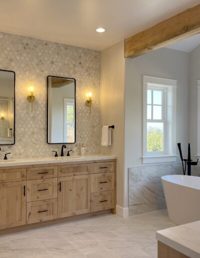 Modern bathroom with wood cabinets, double sinks, two mirrors, a freestanding bathtub, and a large window offering an outside view.